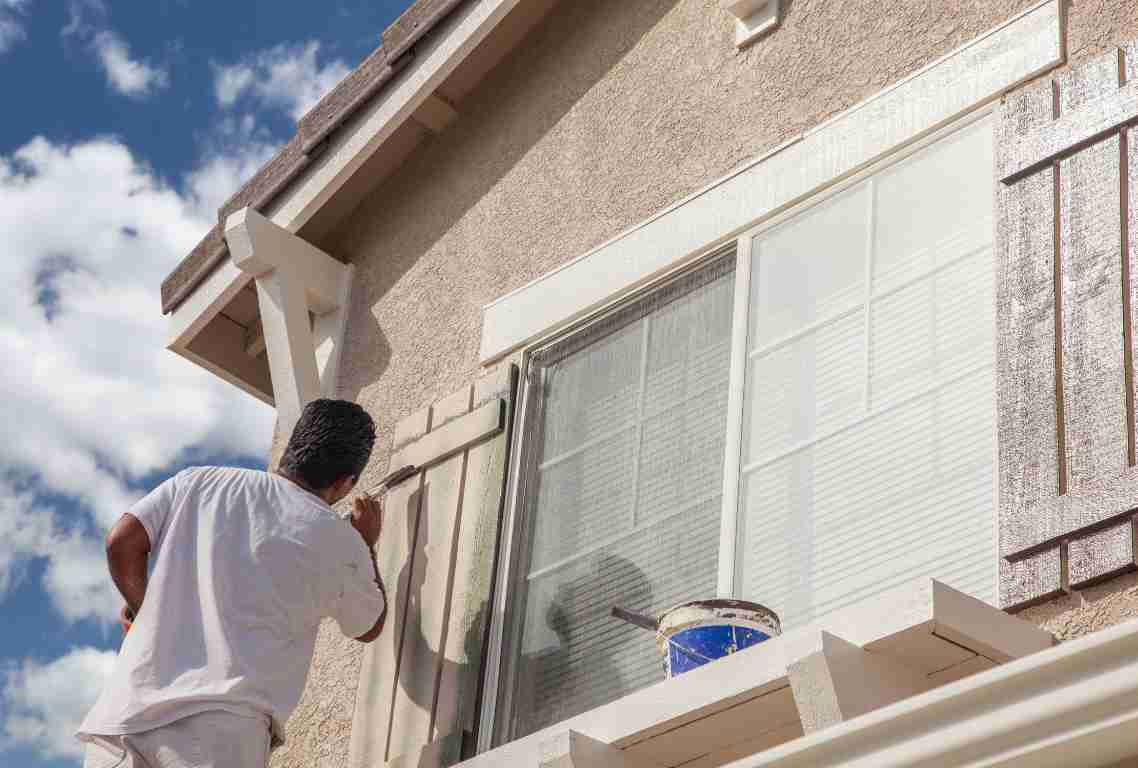 A professional painter painting the exterior of a stucco home